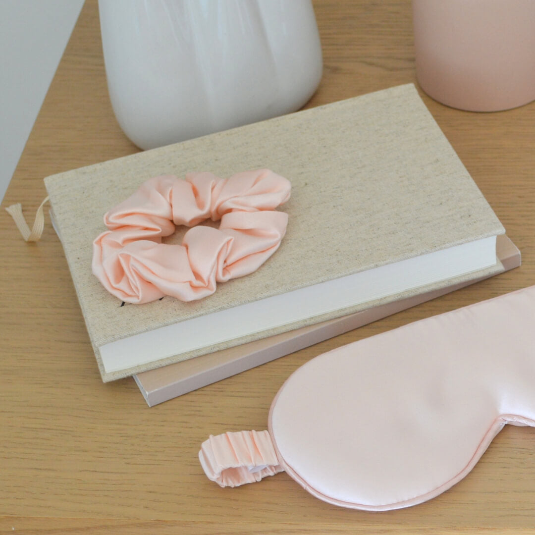 Peach silk hair scrunchie and silk sleep mask in a bedroom interior