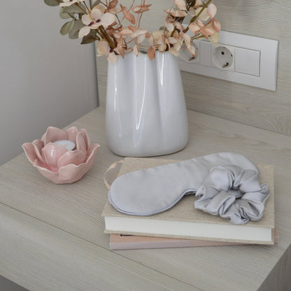 Silver silk hair scrunchie and silk sleep mask in a bedroom interior