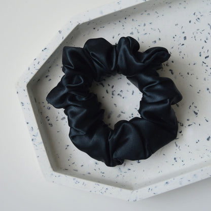 Black silk hair scrunchie displayed in a decorative bowl